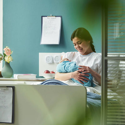 A new mum sits in her bed in hospital, smiling down at her newborn