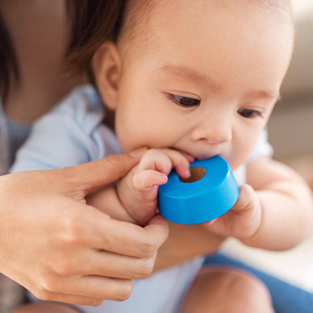 Baby chewing a round toy while being held by their mother
