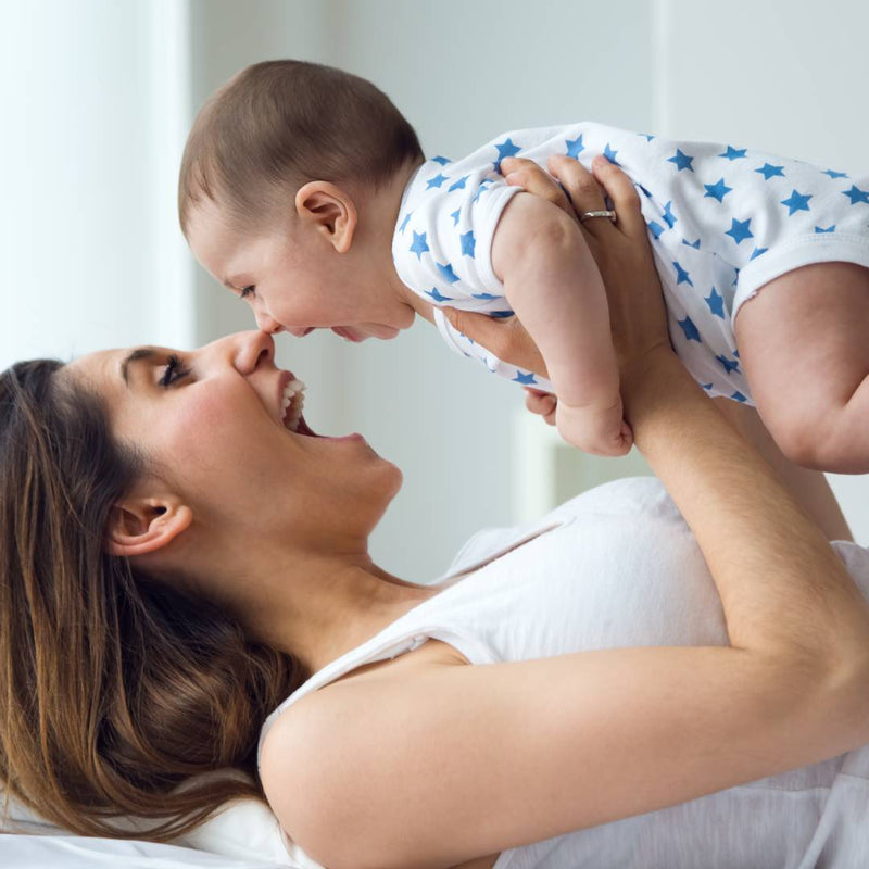 A laughing mother holds her smiling baby above her face 