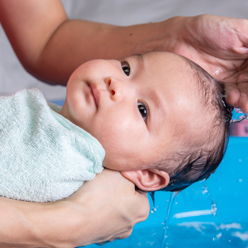 Swaddled newborn baby having their hair washed