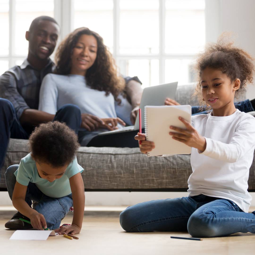 Relaxed family enjoying time together, kids sitting on the floor drawing while parents smile from the couch