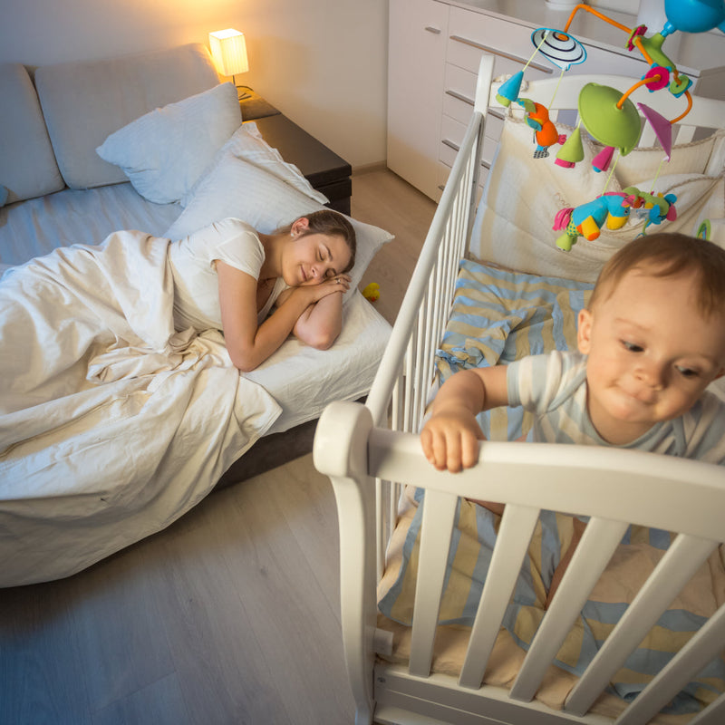 Mother sleeping on a bed next to a baby's cot